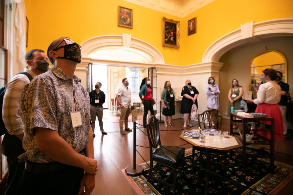 Masked people inside a historic house looking at artifacts.