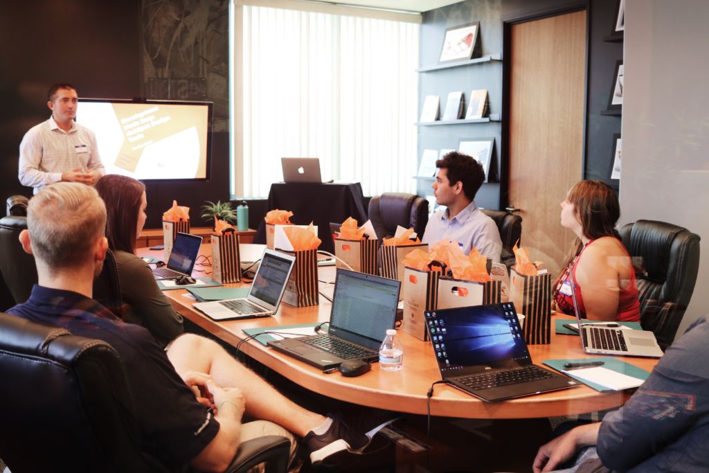 A full board room with people sitting around a table with laptops open.