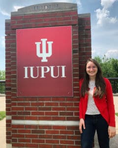 A smiling woman in a red blazer standing in front of an IUPUI sign.