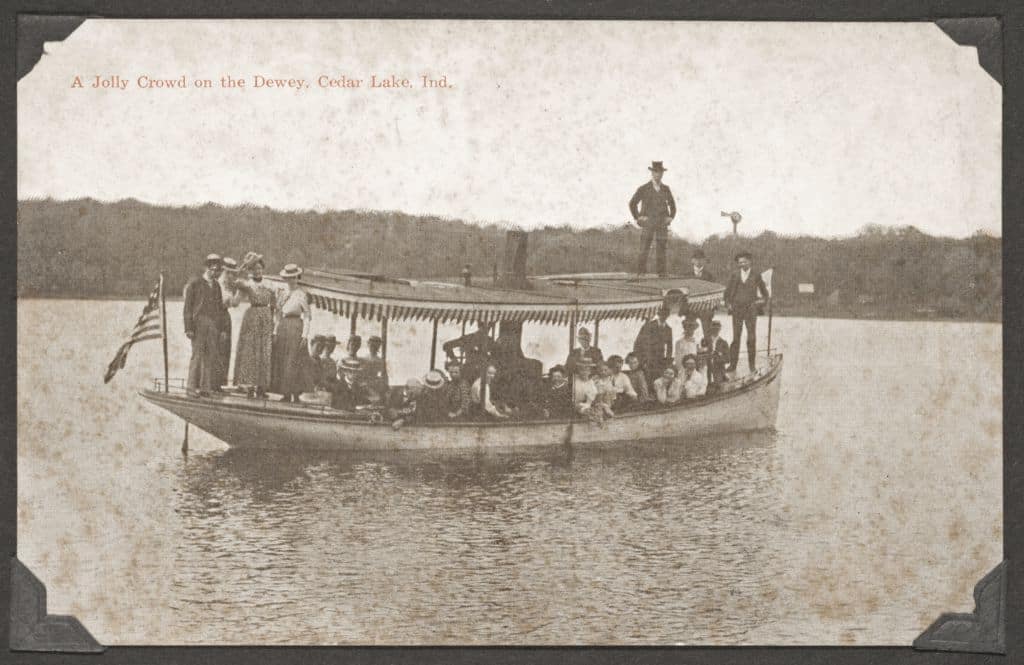 A historic photo of a group of early 20th century people aboard a small boat on a lake.